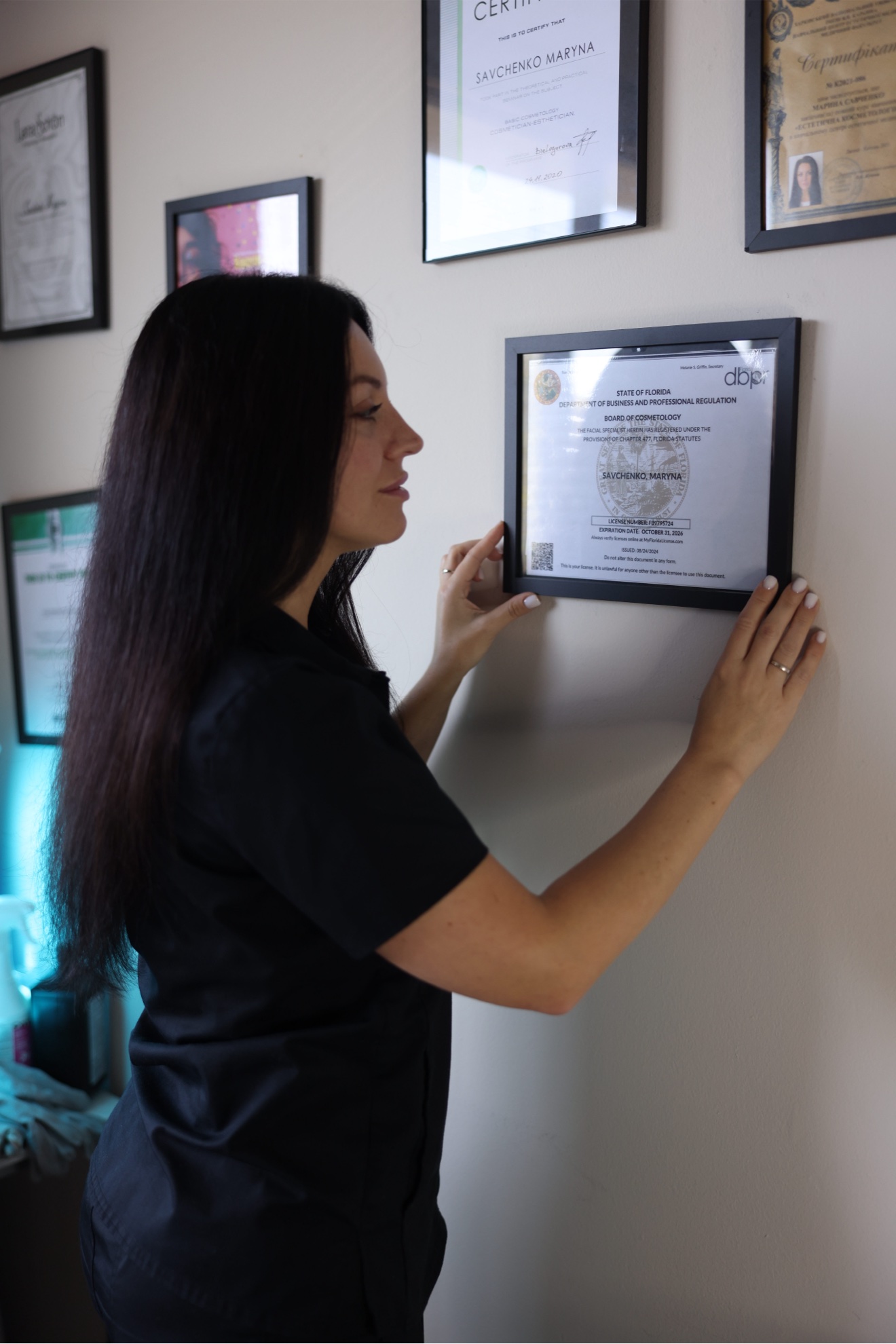 Maryna Savchenko hanging her Florida Facial Specialist license in the studio